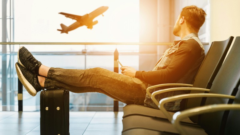 Traveler relaxes at airport while waiting for flight boarding, with plane taking off in background., tags: daten unterwegs - pexel