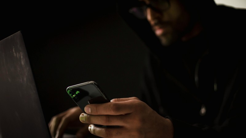 Crop anonymous ethnic male cyber spy with cellphone and netbook hacking system in evening, tags: altes datenleck befeuert - pexel