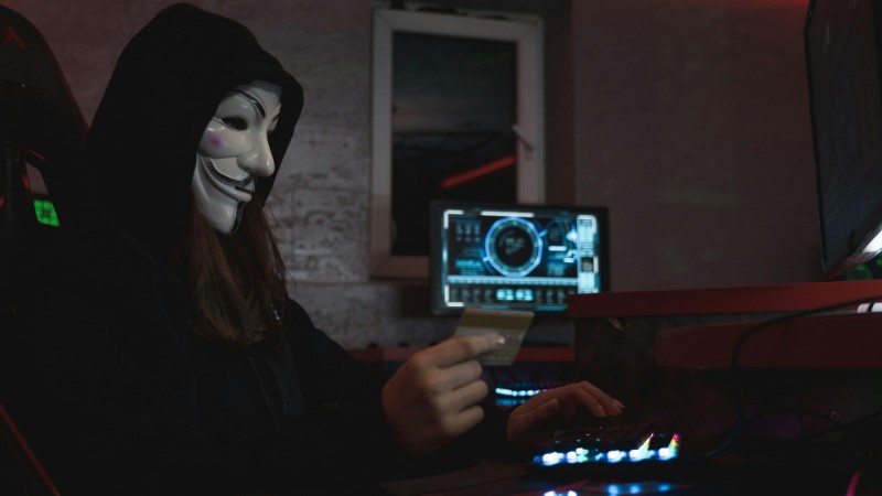 Masked hacker with credit card at computer, symbolizing cybercrime and anonymity., tags: von - pexel